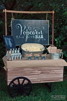 an outdoor popcorn bar is set up in the grass with chalkboard sign above it