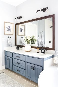 a bathroom with blue cabinets and white counter tops, two mirrors above the sink and flowers in vases on the mirror