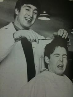 an old black and white photo of two men cutting another man's hair with scissors