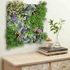 a green wall with flowers and plants on it next to a book, planter and vase