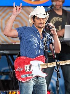 a man with a red guitar on stage at a music festival, giving the peace sign