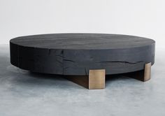 a round wooden table with two brass square bases on it's sides, in front of a white wall