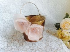 two pink flowers are sitting in a metal bucket on a lace tablecloth next to a flower pot