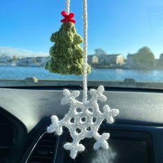 two crocheted snowflakes hanging from the dashboard of a car with water in the background