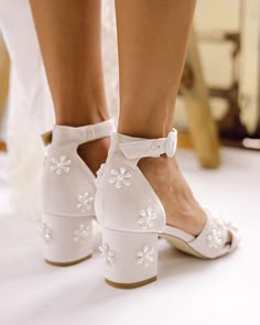 a close up of a person wearing white shoes and high heeled shoes with flowers on them