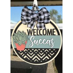 a welcome sign hanging from the side of a window with a black and white checkered bow