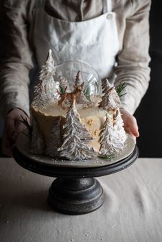 a person in an apron is holding a cake with frosting and trees on it