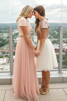 two women standing next to each other in front of a window looking at each other