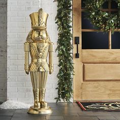 a gold statue is standing in front of a door with greenery on the side