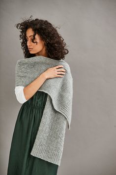 a woman wearing a gray knitted shawl and green dress, with her arms wrapped around the shoulders