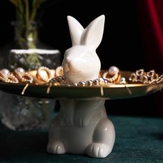 a white rabbit figurine sitting on top of a plate with pearls around it