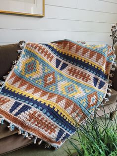 a crocheted blanket is sitting on a couch next to a potted plant