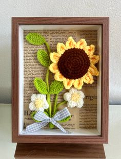 a crocheted sunflower in a shadow box with ribbon and bow on top