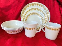 a white and gold dinner set on a red cloth with matching cups and saucers