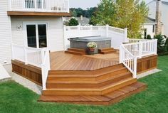 a wooden deck with white railings next to a hot tub on the grass in front of a house