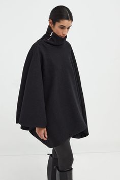 A stylish wool winter cloak, our Avery Cape is the ideal choice for heading out into the cold. Fashioned from Italian virgin wool and offered in fresh neutrals that pair well with any combination of clothing, this women’s wool cape is designed with a loose silhouette. Simple. Elegant. Cozy. Layer her over anything for an instant ready-to-go look. Avery's high collar has a side zipper for style and easy wear. This wool winter cape is lined for added warmth and comfort. | Astrid, in medium grey an Oversized Cashmere Wool Coat For Winter, Elegant Oversized Wool Poncho, Black Cashmere Wool Coat For Winter, Winter Black Cashmere Wool Coat, Funnel Neck Cashmere Outerwear For Fall, Fall Cashmere Outerwear With Funnel Neck, Fall Cashmere Funnel Neck Outerwear, Elegant Wool Poncho For Workwear, Solid Wool Turtleneck Outerwear