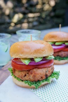 two hamburgers with lettuce, tomato and onion on them sitting on a table