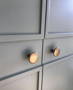 two brass knobs on the side of a white cabinet with grey painted doors and drawers