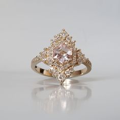 Inspired by the elegance and beauty of chandeliers, this morganite ring features a custom cut hexagon morganite center stone surrounded by natural white diamonds. Tiny white diamonds cascade down the ring band giving it a glamor effect. Made in 14k yellow gold, rose gold and white gold. This ring is handmade and designed in NYC. Materials: - 14K solid gold - 2.5 mm band thickness - 7x7mm custom cut natural hexagon morganite center stone - Natural white diamonds - SI1 clarity white diamonds. Appr Luxury Morganite Diamond Ring With Accents, Luxury Morganite Diamond Ring With Diamond Accents, Luxury Morganite Diamond Ring With Rose Cut, Luxury Morganite Diamond Ring With Rose Cut Diamonds, Morganite Diamond Ring With Accent Stones, Morganite Ring With Diamond Accents, Luxury Morganite Diamond Wedding Ring, Blush Diamond Jewelry With Center Stone, Morganite Diamond Ring With Diamond Accents For Wedding