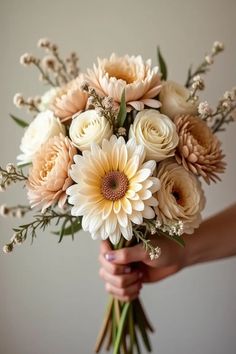 a woman holding a bouquet of flowers in her hands with white and peach colors on the petals