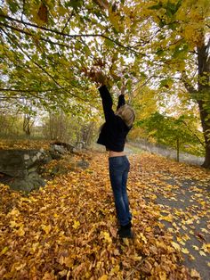 a woman reaching up into the air to grab leaves from a tree with her hands