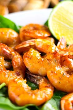 a plate full of shrimp and spinach with lemon wedges next to it on a green leafy surface