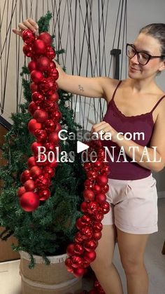 a woman is decorating a christmas tree with red balls and tinsel garlands