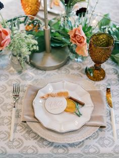 the table is set with plates, silverware and flowers in vases on it