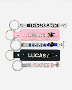 four keychains with the names of three different countries on them, all in pink and black