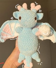 a hand holding a small stuffed animal in the shape of a baby blue and pink dragon