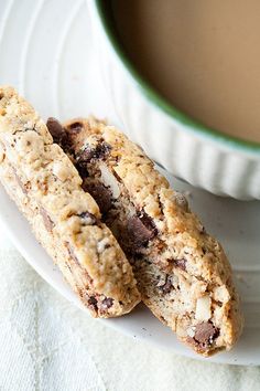 two chocolate chip cookies sitting on top of a white plate next to a cup of coffee