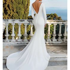 a woman in a white wedding dress standing on a balcony looking at the ocean with her back to the camera