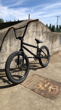 a black bike parked next to a cement wall and drain grate on the ground