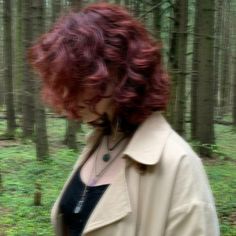 a woman with red hair standing in the woods