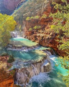 a waterfall in the middle of a canyon with blue water and green trees around it