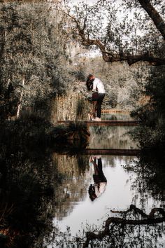 a person standing on a bridge over a body of water with trees in the background