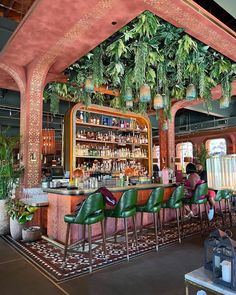 a bar with lots of green chairs and plants hanging from it's ceiling over the bar