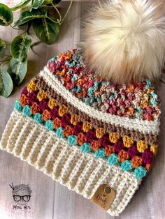 a crocheted hat with a pom - pom sits on a table