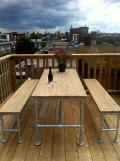 a table and benches on a wooden deck with flowers in the vase next to it