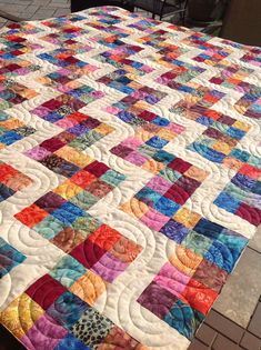 a colorful quilt is laying on a patio table top with a chair in the background