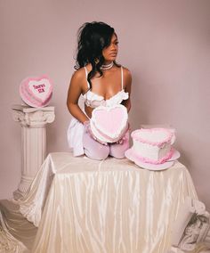 a woman sitting on top of a table next to two cakes