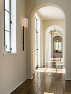 an empty hallway with arched doorways and hard wood flooring