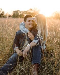 a man and woman are sitting in the tall grass with their arms around each other