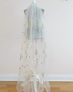 a white veil with flowers on it hanging from a wall next to a wooden floor