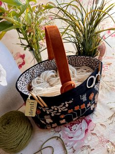 yarn and knitting needles in a basket on a table next to potted plantes