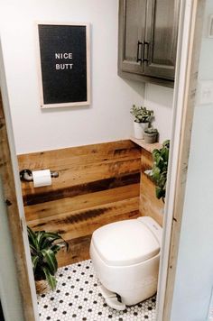 a white toilet sitting inside of a bathroom next to a wooden paneled wall and potted plants