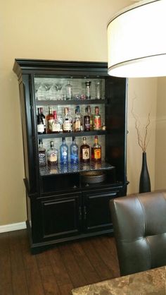 a black cabinet with liquor bottles on it in a living room next to a lamp