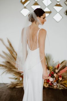 a woman in a white wedding dress with a veil on her head and flowers behind her back