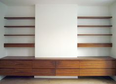 an empty room with shelving unit and wooden flooring on the side, in front of a white wall