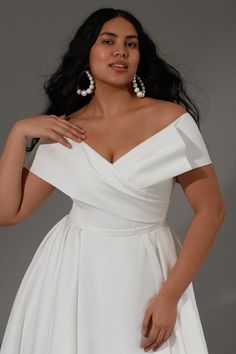 a woman wearing a white dress with pearls on her neck and shoulder, posing for the camera